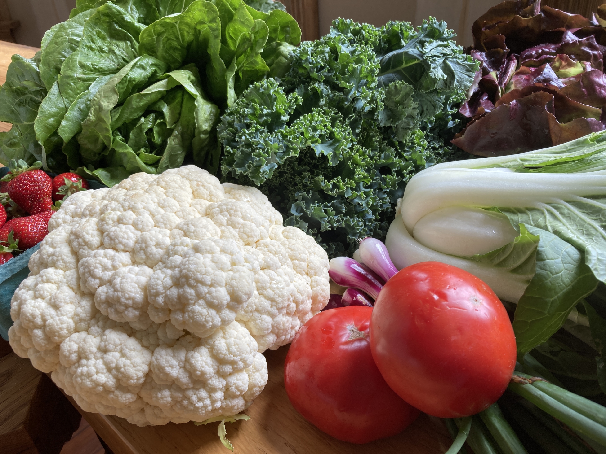 Example of vegetables in a box including celery, green onions, tomatoes, cauliflower, red lettuce, butter lettuce, kale and strawberries.